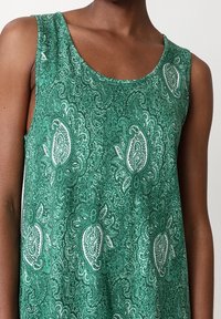 Top sans manches vert en tissu léger avec un motif paisley blanc, doté d'un col arrondi et d'une texture lisse.