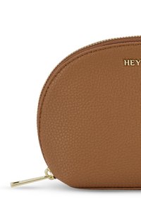 Bruine leren tas met een gestructureerd oppervlak, ronde vorm, gouden rits en een metallic accent met de tekst "HEY" in reliëf.