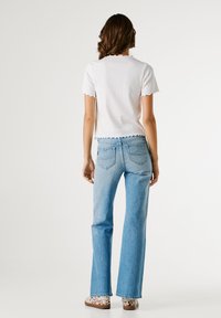 Λευκό τοπ με κοντά μανίκια και κυματιστό τελείωμα, συνδυασμένο με ανοιχτό μπλε καμπάνα τζιν. Τα παπούτσια έχουν καφέ και λευκό σχέδιο με ζωικά μοτίβα.