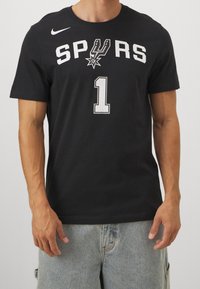Schwarzes Baumwoll-T-Shirt mit "SPURS" in weißen Buchstaben und "1" darunter, ausgestattet mit einem Sternenlogo in der Mitte. Kurze Ärmel, normale Passform.