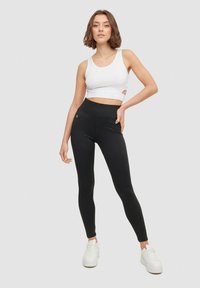 Leggings negras hechas de un tejido elástico con una cintura alta y detalles de bolsillo, combinadas con una camiseta sin mangas recortada blanca y zapatillas blancas.