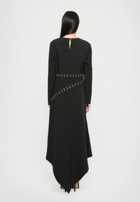 Black long-sleeve dress with a V-shaped hem, features a gold design along the waist and a back keyhole opening. Smooth, textured fabric.