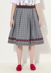 Une jupe plissée en tissu bleu avec un motif floral, une ceinture décorative rouge et noire, et un ourlet inférieur à motifs contrastés.