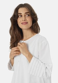 Witte katoenen blouse met een ronde halslijn, knopenrij en driekwartmouwen met gestikte details bij de manchetten.