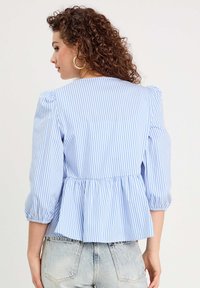 Top peplum a rayas azul y blancas con mangas abullonadas, hecho de una tela ligera, con cintura ceñida y un dobladillo fluido.