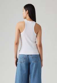 Witte geribbelde tanktop met een ronde hals en brede armsgaten, gecombineerd met lichtblauwe denim jeans met wijde pijpen en een opvallend ontwerp van de achterzak.