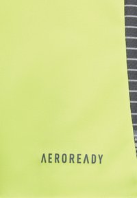 Un tissu jaune vif à la texture lisse présente un panneau rayé gris sur la droite et le logo "AEROREADY" en bas.