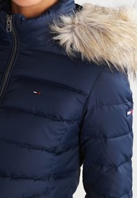 Granatowa kurtka puchowa z futrzanym wykończeniem kaptura, zamek błyskawiczny, pikowane wykończenie oraz mały detal z logo na klatce piersiowej i rękawie.