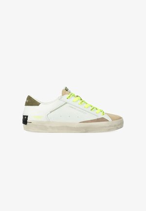 Sneaker bianca low-top con dettagli in suede beige, lacci giallo neon, linguetta posteriore verde e suola bianco sporco leggermente sporca.