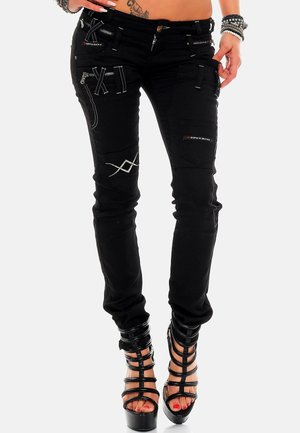 Zwarte jeans met verschillende ritszakken en witte stikselaccenten. Voorzien van een tapered leg ontwerp. Gepaard met hoge hakken met bandjes.