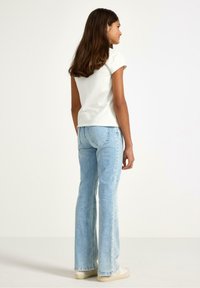 Hvid kortærmet top kombineret med lyseblå vidde jeans. Jeansene har en falmet vask og subtile sømdetaljer. Lærredssko fuldender outfittet.