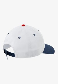 Hvid baseballcap med en navy skygge, rød accent på toppen og blå øjer; justerbar rem bagpå for pasform.