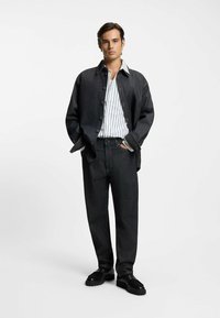 Giacca di denim scuro sopra una camicia bianca a righe, abbinata a jeans scuri a vita alta e scarpe platform nere. Texture liscia, dettagli con bottoni.