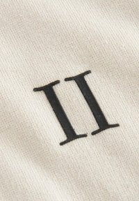 Gros plan du chiffre romain noir II imprimé sur un tissu beige texturé.