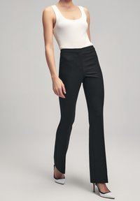 Pantalons noirs évasés en tissu texturé, associés à un débardeur blanc ajusté à côtes et des escarpins noirs et blancs pointus.