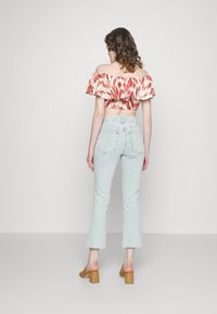 Top cropped ombro a ombro em vermelho e creme com efeito tie-dye, com mangas franzidas, emparelhado com jeans flared em azul claro. Sapatos bege de salto bloco.