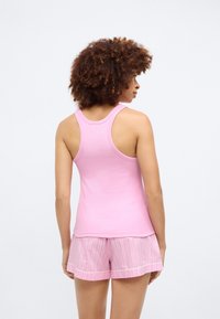 Ροζ βαμβακερή μπλούζα με σχέδιο racerback, συνδυασμένη με ανοιχτό ροζ σορτς με ρίγες και αντίθετο στρίφωμα. Απαλή υφή, άνετη εφαρμογή.