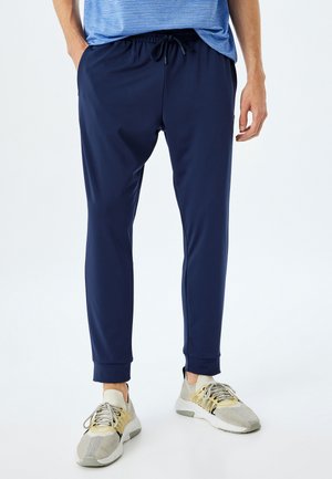 Marine træningsbukser med elastisk talje og snor. Lavet af glat stof, med tapered ben og ribbede manchetter. Båret med lyse sneakers.