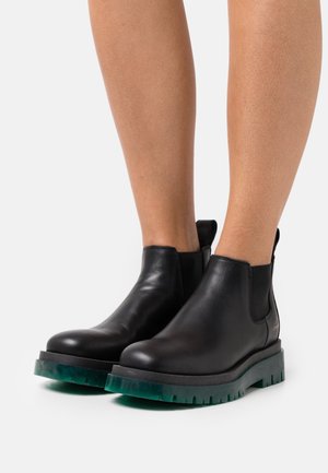 Bottes Chelsea en cuir noir avec panneaux latéraux élastiques et semelle en caoutchouc verte translucide épaisse, dotées d'une finition lisse et de languettes pour faciliter l'enfilage.