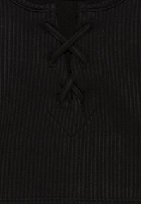 Zbliżenie na czarną żeberkowaną tkaninę z detalami sznurowania, w której grube czarne sznurki przewleczone są przez oczka.