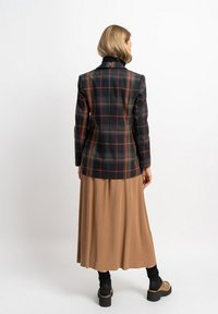 Schwarze Karoblazer mit orangefarbenen Akzenten, getragen über einem beigen Faltenrock. Mit einem kontrastierenden schwarzen Kragen und klobigen Schuhen.