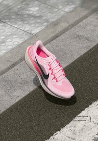 Ružová športová obuv s priedušným zvrškom, čiernym logom swoosh, bielou podrážkou a ružovými šnúrkami. Zaujímavá pre svoj textúrovaný vzor a štíhly dizajn.