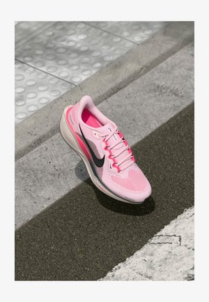 Vaaleanpunainen urheilujalkine, jossa on verkkopäällinen, musta swoosh-logo, valkoinen pohja ja vaaleanpunaiset nauhat. Erityinen rakenne ja virtaviivainen muotoilu tekevät siitä huomattavan.