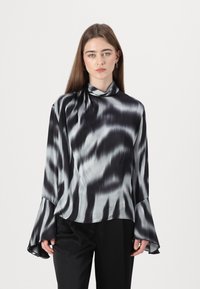 Blomst med svart og sølv tie-dye mønster, høyt halskutt, bredde-ermer, glatt satengstoff og avslappet passform. Kombinert med svarte bukser.