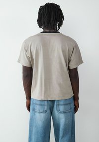 Korte mouwen beige T-shirt met een ronde hals, gecombineerd met lichtblauwe denim jeans met opvallende achterzakken en vervaagde details.