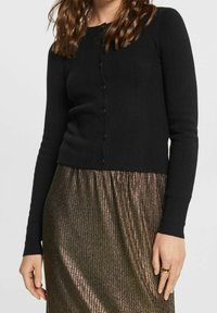 Zwarte geribbelde cardigan met lange mouwen en ronde hals, voorzien van een knoopsluiting aan de voorkant en een cropped zoom, gecombineerd met een metallic geplooide rok.