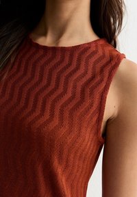 Top senza maniche color ruggine con un motivo a zigzag testurizzato, realizzato in un materiale a maglia. Collo liscio e silhouette aderente.