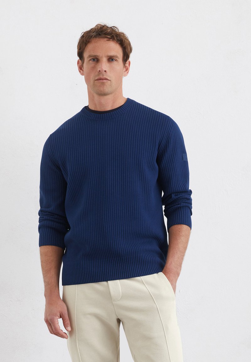 Marineblauwe geribbelde trui met lange mouwen en ronde hals, met een gestructureerde stof en een klein accentdetail op de linkermouw.