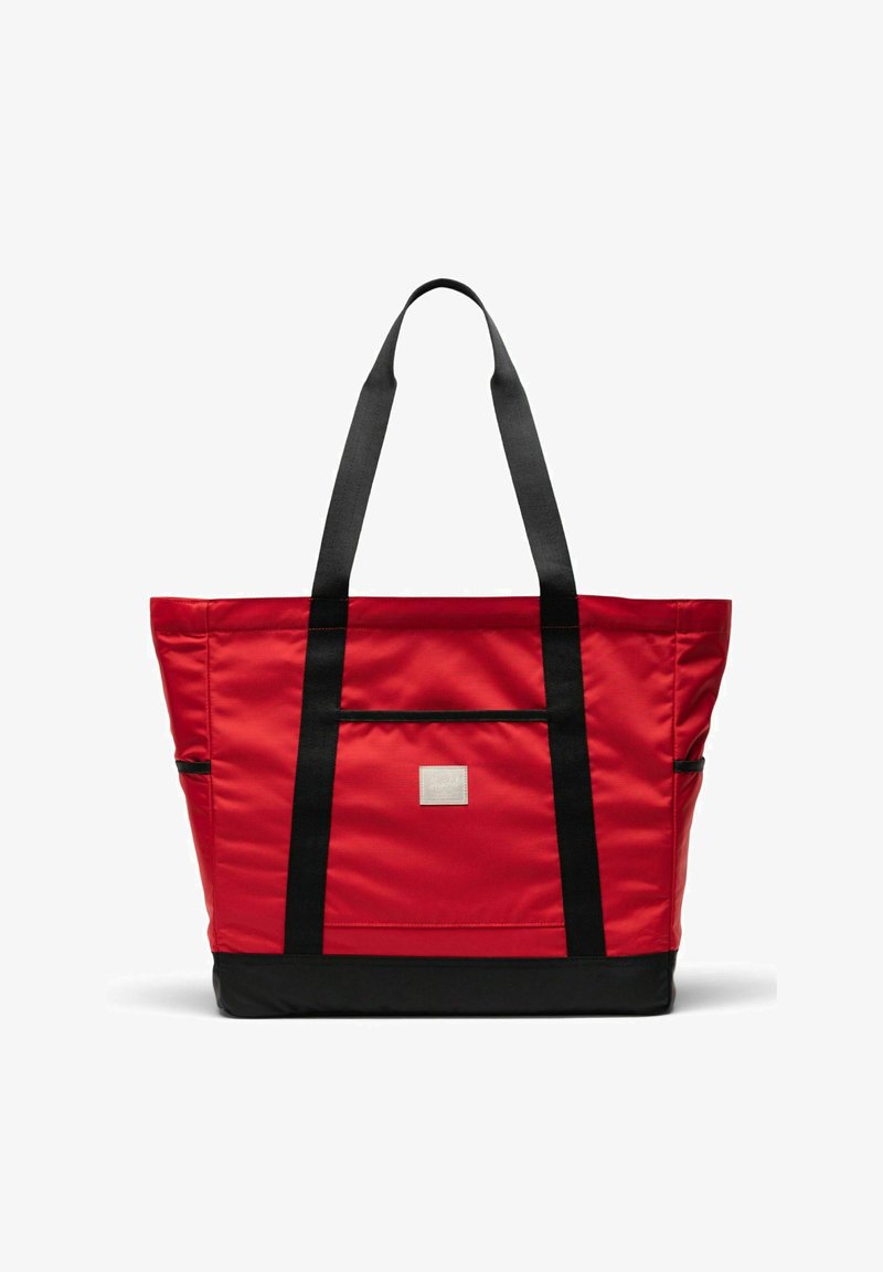 Sac fourre-tout rouge avec des poignées et une base noires, une poche avant et une petite étiquette rectangulaire au centre sur fond blanc.