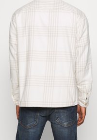 Witte flanellen overhemd met lichtbeige ruitpatroon, voorzien van lange mouwen en knoopmanchetten. Zachte textuur en een relaxed fit.