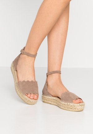 Brown suede espadrilles with a scalloped upper design, ankle strap with a buckle, and jute-wrapped wedge heel. Open-toe style.