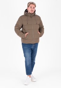 Brązowa puchowa kurtka z kapturem, z zamkiem z przodu, dwoma bocznymi kieszeniami i wzorzystą podszewką w kratę. Połączona z niebieskimi dżinsami i białymi sneakersami.