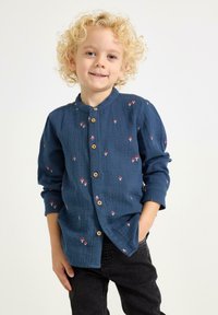 Blå skjorta med knappupptäckning och mandarin krage, prydd med blommig brodyr och träknappar. Tillverkad av texturerad tyg, långa ärmar.