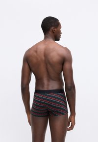 Boxeri pentru bărbați, de culoare neagră, cu un model în zig-zag în roșu și alb. Talie elastică. Materialul pare neted și elastic.