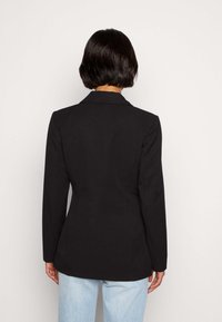 Černý saka s klopovými límci, dlouhými rukávy a těsným střihem; zadní část má hladkou texturu a čisté linie.