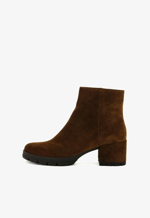 Stivale alla caviglia in suede marrone con tacco a blocco, punta rotonda, texture liscia e design minimalista. Suola in gomma per aderenza e durata.