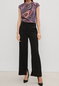 Kurzärmliges Oberteil mit einem pink-blauen Wirbelmuster; kombiniert mit hochtaillierten, schwarzen, weit geschnittenen Hosen mit Seitenschlitzen und glatter Textur.