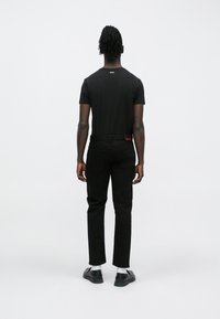 Μαύρο μπλουζάκι με λογότυπο στην πλάτη, συνδυασμένο με μαύρο παντελόνι και μαύρα παπούτσια, με λευκές κάλτσες για αντίθεση. Απλός σχεδιασμός, ελάχιστες λεπτομέρειες.