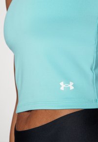 Débardeur bleu clair ajusté en tissu lisse, avec un logo blanc en bas à droite. Le design comprend une coupe courte et une texture côtelée.