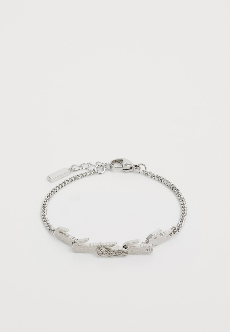 Srebrna narukvica s lancem koja sadrži veze u obliku krokodila s teksturiranim detaljima. Zaključavanje s kopčom na jednom kraju, minimalistički dizajn u cjelini.