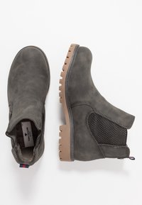 Pár šedých kotníkových bot s robustními béžovými podrážkami, elastickými bočními panely a textilními poutky, zobrazených z vrchu a z boku na bílém pozadí.