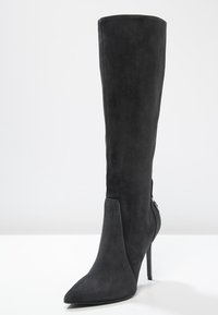 Bota de tacón stiletto alta de ante negro con puntera afilada, textura suave y detalle decorativo en la costura lateral. Presenta un tacón delgado y alto.