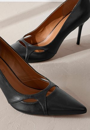 Schwarze Leder-Pumps mit spitzen Zehen und Ausschnitten, die eine glatte Textur und einen schmalen Stiletto-Absatz aufweisen.