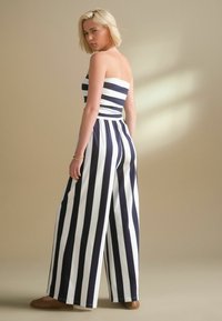 Randig jumpsuit med en strapless topp och vida ben. Har marinblå och vita vertikala ränder, tillverkad av bomull, med en flödande textur.
