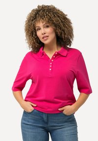 Fuchsia polo shirt met een kraag, halve mouwen en vijf knopen bij de hals. Gemaakt van een gladde stof, gecombineerd met blauwe denim jeans.