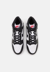 Black and white high-top sneakers with perforated toe, black leather accents, and red logo detail on tongue. Features black laces and strap.